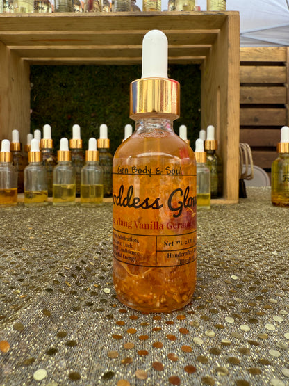 ottle of Goddess Glow Body Oil with ylang, vanilla, and geranium, displayed on a sparkling gold table.